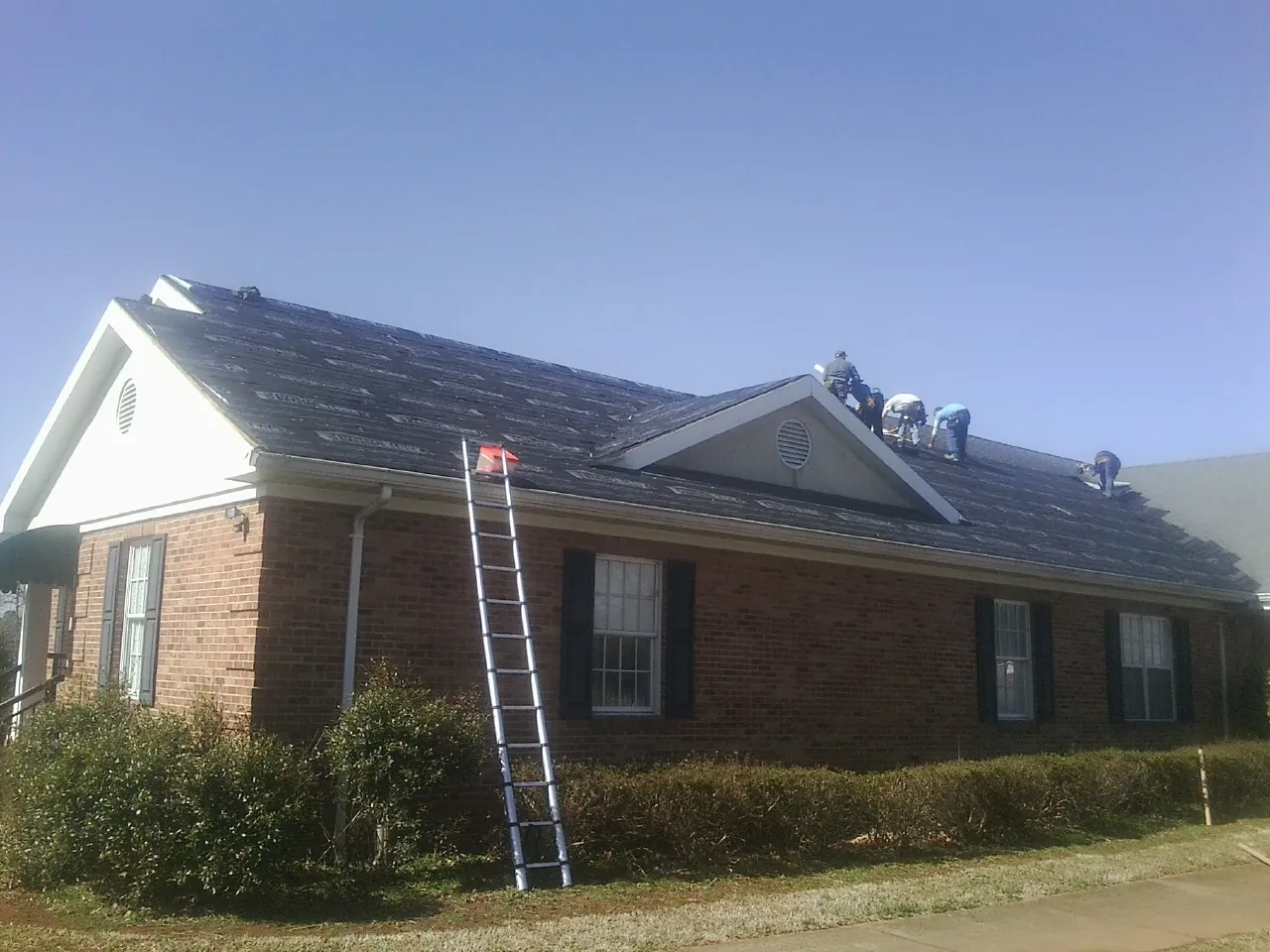 Crew tearing shingles off a brick ranch roof with a ladder set — Emergency Roof Repair work by our crew in Hermitage