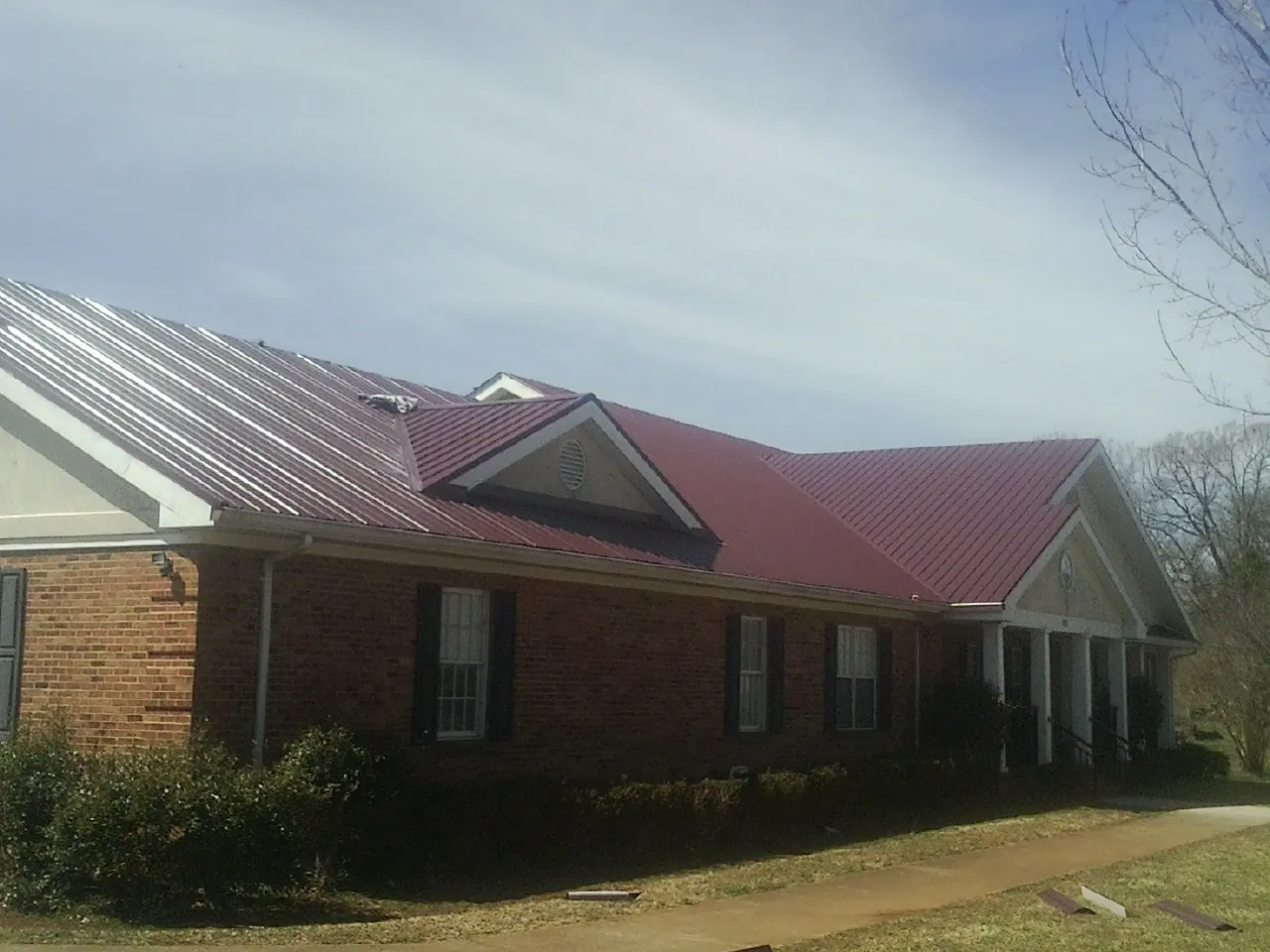 Red metal roof with gabled entries on a long brick building, from a Hail Damage Roof Repair job in Hermitage
