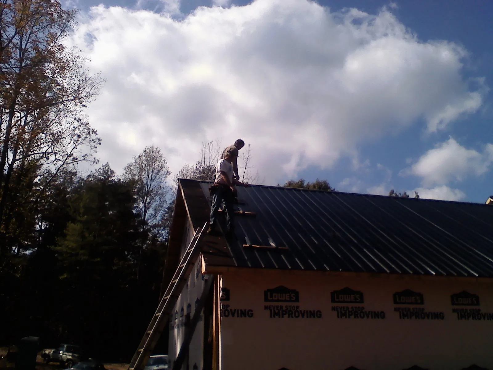 Roofer fastening dark metal panels high against a cloudy sky, from a Roof Inspection job in Hermitage