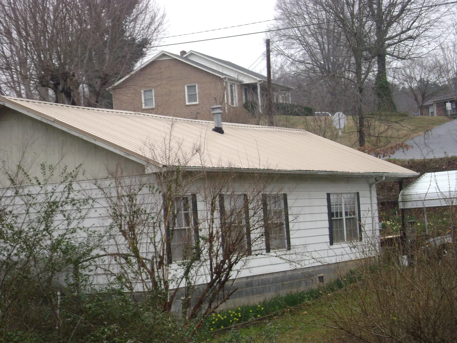 Tan metal roof on a white sided house set into a hillside — Commercial Roofing by Roofing Brothers in Hermitage
