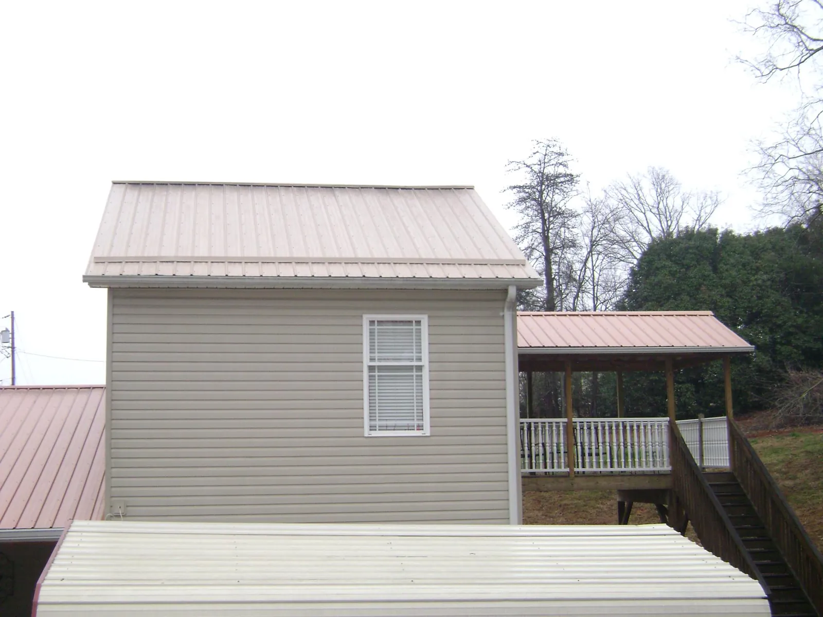 Tan metal roofs on a two story addition and attached porch, from a Roof Replacement job in Hermitage